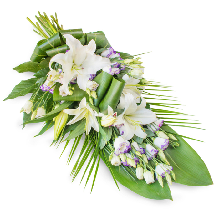 A beautifully composed funeral floral sheaf lies diagonally across a stark white backdrop, its elegant teardrop form clearly defined from the fuller gathering of stems at the upper end to the slender, pointed finish below. The focal point is a group of white oriental lilies, some in full bloom, their open, trumpet-shaped flowers displaying creamy petals and delicate yellow-green stamens, others still held in elongated buds that add height and a sense of quiet anticipation. These lilies are interspersed with sprays of lisianthus, whose smaller, bell-shaped blossoms are predominantly white but gently traced with lavender and pale purple at the petal edges, like a soft wash of colour over the sky above Worcester Park in the late afternoon. This restrained palette of whites and subtle purples creates a mood that is both serene and deeply respectful. Cradling the flowers is a generous array of greenery. Broad, dark green leaves provide a strong, almost architectural foundation, while fine, palm-like fronds extend from one side and downwards, accentuating the elongated silhouette and imparting a natural, flowing movement. Some leaves are expertly rolled and folded near the centre and upper portion of the spray, introducing sculptural lines that demonstrate a florist's considered craftsmanship. Imagined in person, the petals would feel smooth and satiny, the foliage cool and slightly waxy, and the overall fragrance lightly floral with the clean freshness of lilies and cut stems. This style of arrangement suits funerals, remembrance services, or wakes held in Worcester Park and the surrounding neighbourhoods, offering a calm presence and a tangible expression of sympathy and honour.
